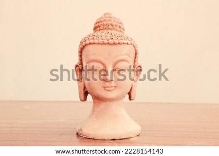 The head of a meditating Buddha on a pinkish-beige light background. Full face.