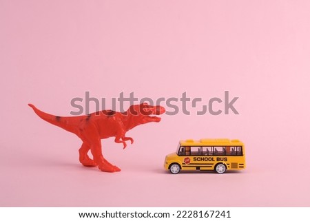 Toy two dinosaur tyrannosaurus rex with school bus on pink background. Minimalism creative layout
