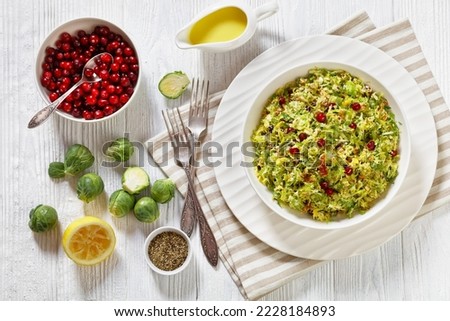 brussels sprouts slaw with almonds, crunchy fried bacon and cranberries in white bowl on wooden table with ingredients, horizontal view from above, flat lay Royalty-Free Stock Photo #2228184893