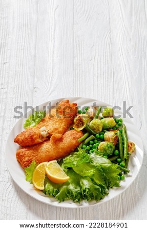 Crispy Beer Batter Cod Fish fillet with roast brussel sprouts, green beans, green peas and fresh lettuce on white plate on wood table, vertical view from above,  free space