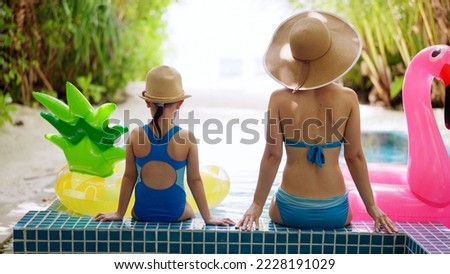 Rear View Of Woman And Child Sitting At The Edge Of Swimming Pool