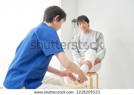 Asian nurse bandaging a patient's ankle