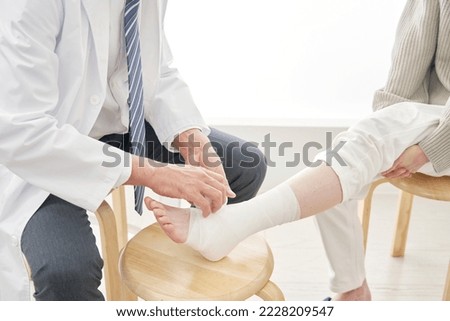 Asian doctor bandaging a patient's ankle, no face