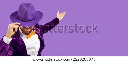 Ladies and gentlemen, welcome. Funny guy inviting you to a party. Handsome man in a fedora hat bows his head as he's showing and presenting something on a blank empty solid purple copyspace background Royalty-Free Stock Photo #2228209875