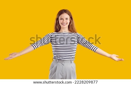 Portrait of a happy, glad, cheerful, positive, friendly woman with a kind, sincere, toothy smile standing on a yellow studio background, spreading her arms wide open to hug you and give a warm welcome Royalty-Free Stock Photo #2228209877