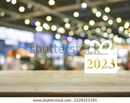 Gift box happy new year 2023 flat icon on wooden table over blur light and shadow of shopping mall, Business shop online concept
