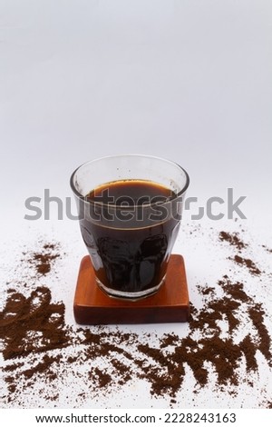Photo of black coffee with coffee grounds sprinkled around it. Isolated on white background
