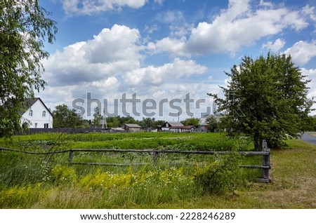 Beautiful summer european rural landscape. Village houses and fence against blue sky background with cumulus clouds