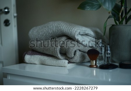 a plie of sweaters in brown and beige colors on white dresser, by a potted green philodendron plant
