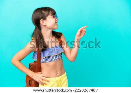 Little caucasian kid going to the beach isolated on blue background pointing finger to the side and presenting a product