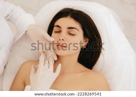 Lip augmentation procedure. Syringe near the woman's mouth. Injections to increase the shape of the lips. Cosmetologist makes injections for lip augmentation. 