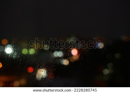 Raindrops on the window glass and unfocused lights of a night or evening city. Background of the night city behind the glass during the rain