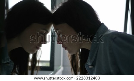 Anxious woman looking at her own reflection at bathroom mirror feeling regret and preoccupation Royalty-Free Stock Photo #2228312403