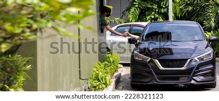Hand Man in car receiving coffee in drive thru fast food restaurant. Staff serving takeaway order for driver in delivery window. Drive through and takeaway for buy fast food for protect covid19. Royalty-Free Stock Photo #2228321123