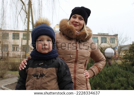 Mom and her little son are walking down the street in the countryside in winter. A little boy in a warm jacket and a winter hat