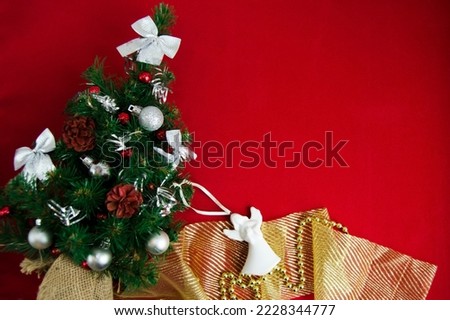Christmas tree, white angel, golden ribbon and Christmas decorations on red background, flat lay. Space for text
