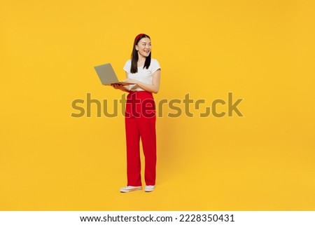 Full size body length bright young girl woman of Asian ethnicity 20s years old wears casual clothes hold use work on laptop pc computer look back isolated on plain yellow background studio portrait
