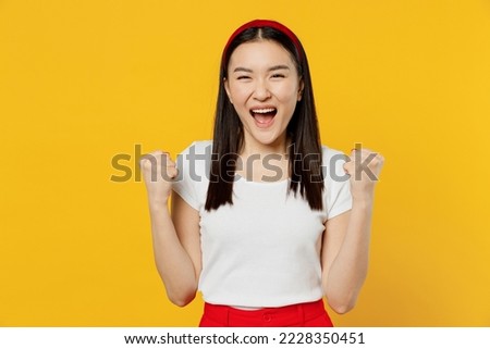 Amazing excited fancy young girl woman of Asian ethnicity 20s years old wears white t-shirt doing winner gesture celebrate clenching fists say yes isolated on plain yellow background studio portrait Royalty-Free Stock Photo #2228350451
