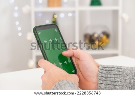 A man holds a phone in an upright position with a green screen. Phone with chromakey. Copy space. The concept of advertising, New Year's holidays, Christmas.