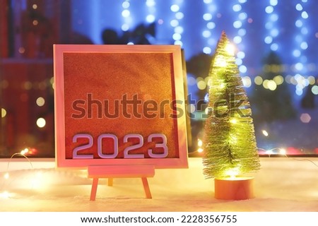 The numbers new year 2023 on a beautiful easel next to Christmas tree and lamp. Discounts, promotions for hotel reservations for the new year 2023 and Christmas. Sale 2023. Production calendar 2023.