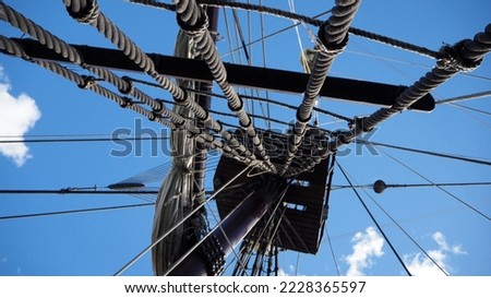Bottom view of a ship mast with white sails, ropes and yards  against a blue sky with sunny day clouds. Marine concept.
