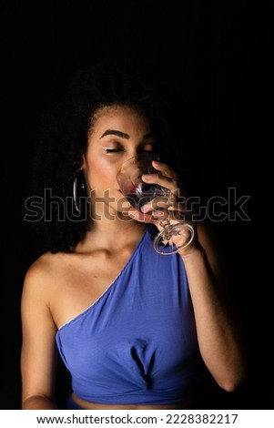 Portrait of young woman drinking water from a glass cup. Isolated on black background in studio