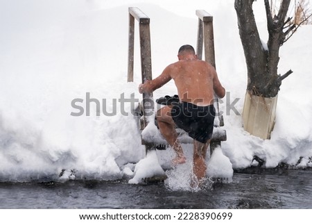 A man comes out of the ice hole after a swim. He climbs the icy steps of a wooden staircase. Icy water drips from the body. Selective focus.                  