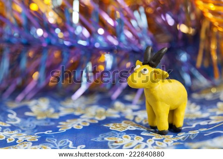Plasticine world - little homemade yellow goat with black horns and hooves on purple background, selective focus and place for text 