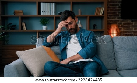 Tired upset father caucasian bearded man sit on sofa frustrated about hard working day at home stressed worried single guy lonely male irritated anxious feel unwell exhaistion lack of energy stress Royalty-Free Stock Photo #2228424485