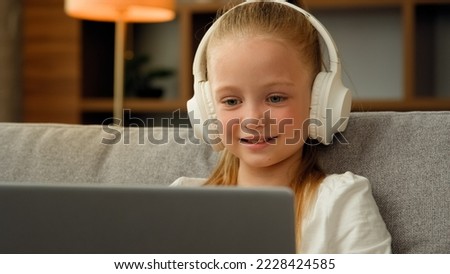 Beautiful kid child little gamer studying online on laptop at home listen audio music in headphones playing computer game laughing pretty girl watch funny cartoons use electronic device resting alone