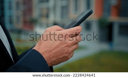 Unknown millennial man entrepreneur standing outside holding in hands modern gadget using mobile device for business communication online texting message in web chat checking corporate email on phone