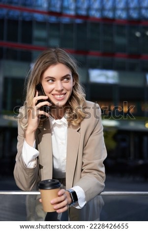 Vertical shot of smiling businesswoman answer mobile phone call, talking on smartphone and drinking coffee.