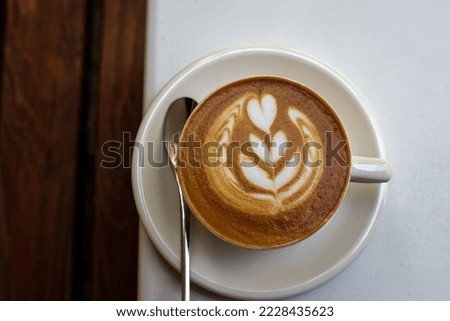 white cup of cappuccino with latte art on white table wooden background. Hot drink at cafe. Top view