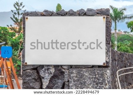 Mockup of a laminated poster screwed to a stone wall with screws in a city park in Puerto de la Cruz, Spain. Blank banner template with rules of conduct in the park, garden, beach, playground, etc.