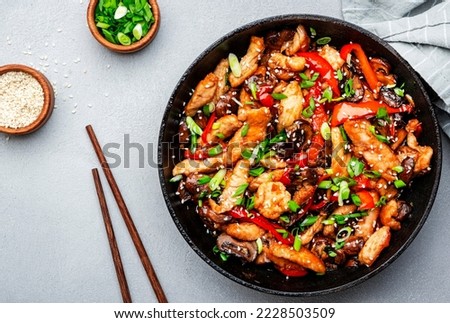 Stir fry with chicken, red paprika, mushrooms and chives in frying pan. Asian cuisine dish. Gray kitchen table background, top view, copy space Royalty-Free Stock Photo #2228503509
