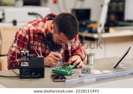 Electronics engineer man repairing computer part in service center. Fixing service in lab. Concentrated while working.Electronics repair service. It technician soldering circuit board in a workshop. Royalty-Free Stock Photo #2228511491