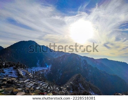 scenery of snow with bright sun in the background and mountains making this picture incredibly amazing moreover the small houses add more beauty to the picture.
