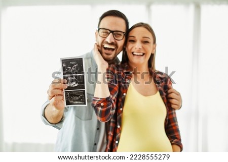 Happy young couple, pregnent woman, holding and showing ultrasound scan picture at home