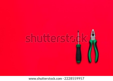 Quality green building pliers and screwdriver tools for repair a car or house on red background. Do it yourself instrument. Banner for advertising construction shop with copy space. Business card.