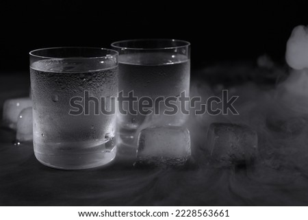 Vodka in shot glasses with ice on table against black background, closeup