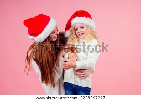 ,happy redhead ginger woman and cute little blonde girl wearing santa claus hat and having fun together in studio pink background