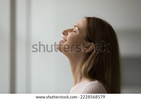 Close up shot side profile face view of beautiful young 30s blissful woman enjoy pleasant fragrance, breathing fresh conditioned air inside room, closing her eyes dreaming feeling happy and peaceful Royalty-Free Stock Photo #2228568579