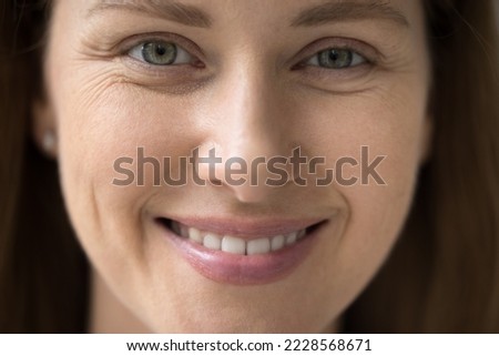Cropped close up part of female face front view, young 30s woman portrait look at camera, having white-toothed smile, wrinkles around eyes, staring at you. Natural beauty, advertise skincare treatment Royalty-Free Stock Photo #2228568671