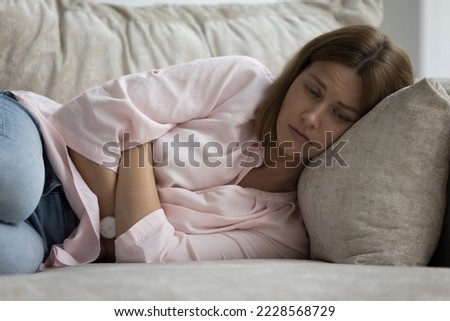 Upset young woman lost in thoughts, feeling lonely or unhealthy lying on sofa alone at home, thinking about relationship or personal problems. Mourning, yearn, suffers after miscarriage or abortion Royalty-Free Stock Photo #2228568729