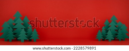 Christmas funny childish background with paper green spruce forest on saturated festive red backdrop in modern minimalist style, copy space, vertical. New year season banner mockup for web, design.