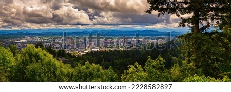 Large panorama of Portland skyline in Oregon under heavy clouds photographed from Pittock Mansion viewpoint.