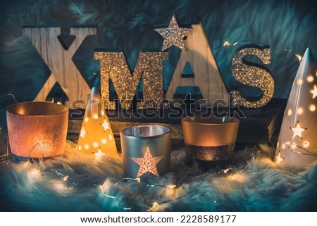 Word xmas in wooden capital letters, uppercase, and different christmas candle lights and fairy lights on a fur  Royalty-Free Stock Photo #2228589177