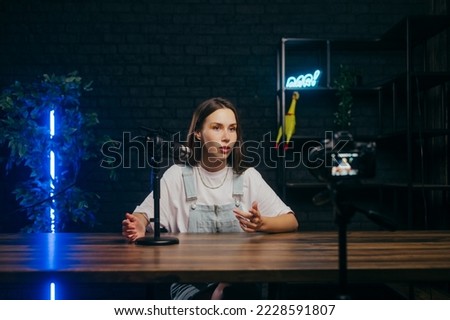 Beautiful lady is recording talking videos into the microphone, looking at the camera with a serious face. Creation of professional content by bloggers.