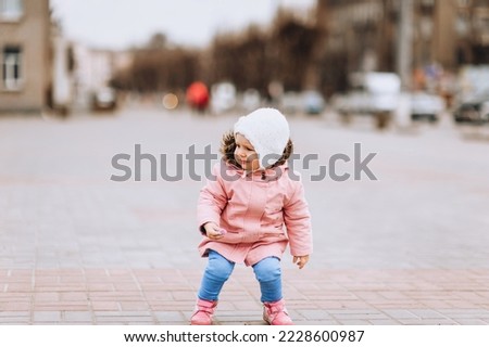A little girl, a child of preschool age, walks in the city and draws on asphalt, tiles with multi-colored chalk. Photography, childhood.