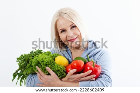 Happy woman with blond hair an beautiful smile holds a bag of vegetables and herbs red pepper and green lettuce in her hands for a healthy diet with vitaminswith. Concept healthy food vegetable